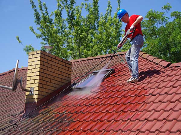 House roof cleaning with pressure tool. Worker on top of building washing tile with professional equipment. Moss removing with water.