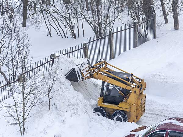 A small city excavator is used for local processing of city roads. Fighting heavy snow.